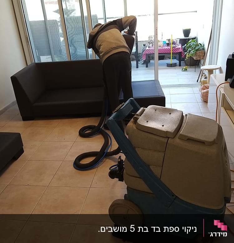 אדם מנקה ספה עם מכונת ניקוי מקצועית